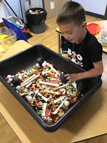 A child looking in a sensory bin filled with Halloween themed items