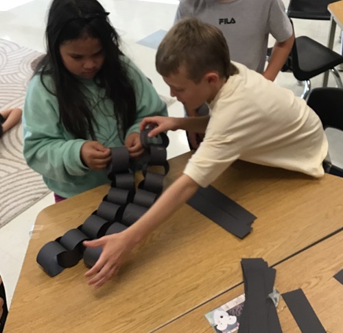 Children at a table adding construction paper loops to make a spider's legs