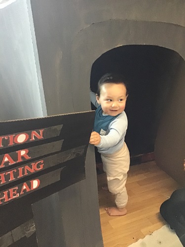 An infant standing up inside the cardboard cave