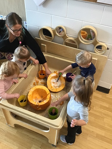 An educator and children exploring the insides of a pumpkin