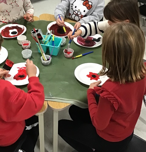 Children sitting at a table painting red poppies on paper plates