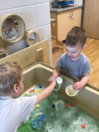 Two children working together to scoop water into a cup