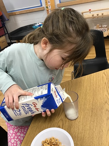A child sitting at a table pouring milk into a cup