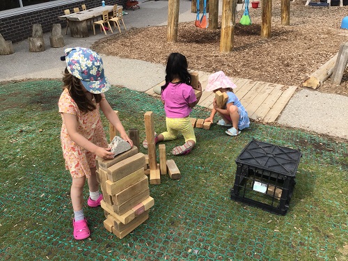 Children using large wooden blocks outside on the playground