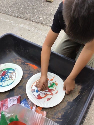 A child sprinkling colourful sand onto glue on a paper plate 