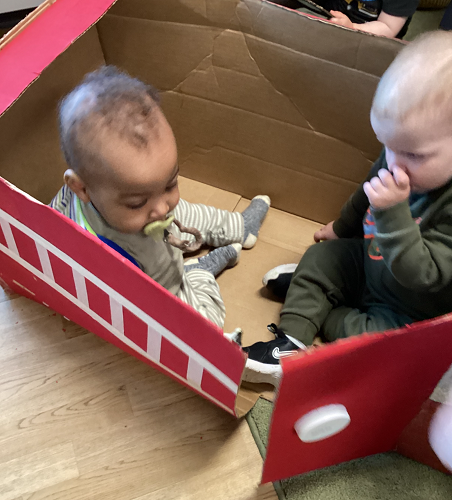 Two children sitting in a cardboard box fire truck