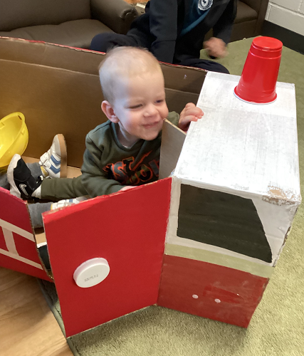 A child sitting in a cardboard box fire truck