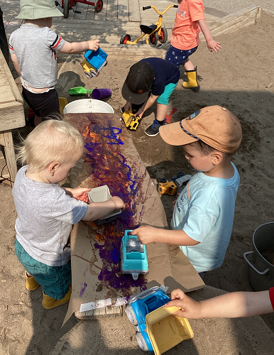 Children pushing cars down a ramp through paint
