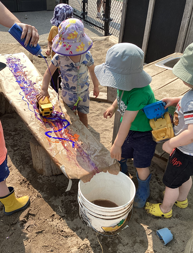 Children pushing cars down a ramp through paint