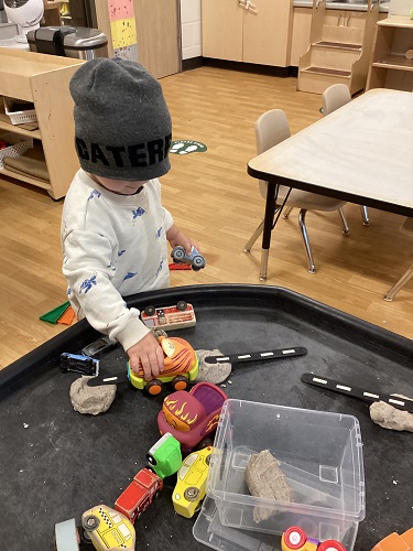A child at the tuff tray driving cars over balls of playdough and popsicle stick ramps