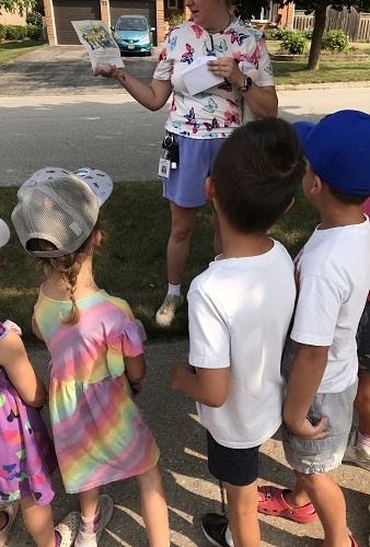 An educator reading a part of a story to a group of children outside on the sidewalk