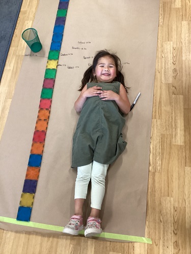 A child laying on the brown paper next to magnet tiles being measured 