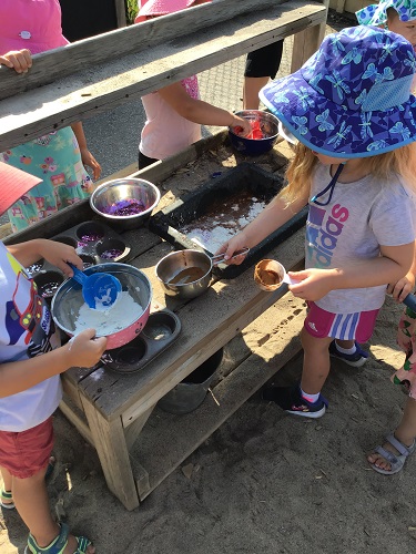 Children at a mud kitchen mixing sand and flour in bowls