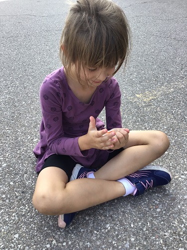 A child sitting on the blacktop with a ball of playdough in their hands