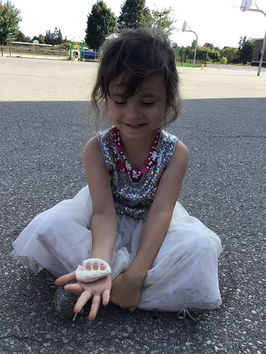 A child sitting on the blacktop with a ball of playdough in their hands