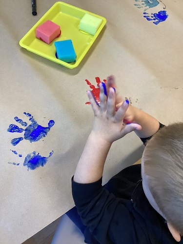 A child at a table rubbing his hands together that have paint on them