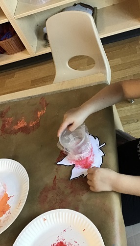 A child at a table painting a leaf