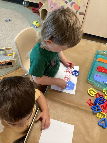 Children sitting at a table using alphabet cookie cutters and paint
