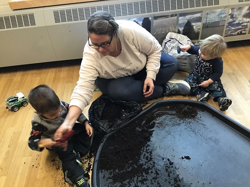 An educator and children sitting on the floor scooping soil