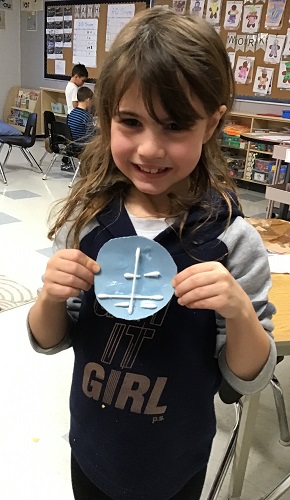 A child holding up a handmade snowflake on construction paper
