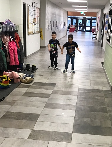 Two children participating in paper plate skating in the school hallway
