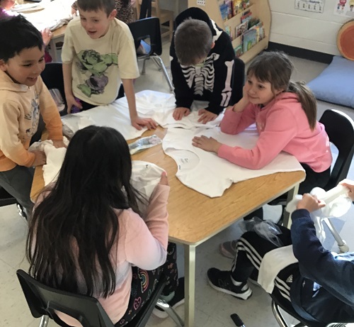Children at a table with shirts layed out in front of them