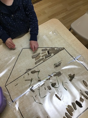 A child sticking wooden pieces to a Mac-Tac house