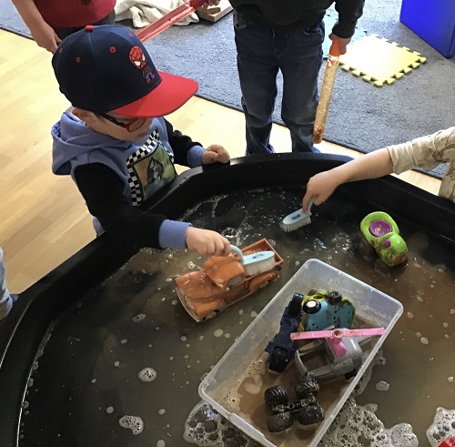 Children using brushes to wash the mud off the toy cars and trucks at the Tuff Tray