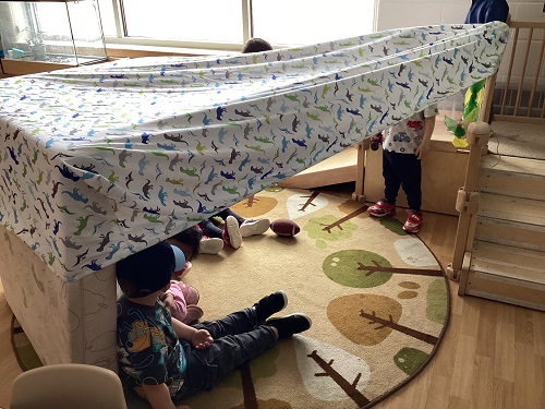 Children hiding under a sheet fort in the classroom