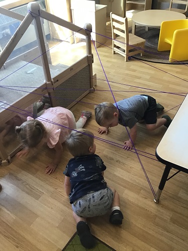 Children crawling under and through string tied around the table and climber