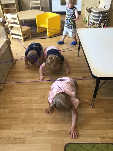 Children crawling under and through string tied around the table and climber