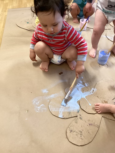 An infant painting on a cardboard flower on the floor