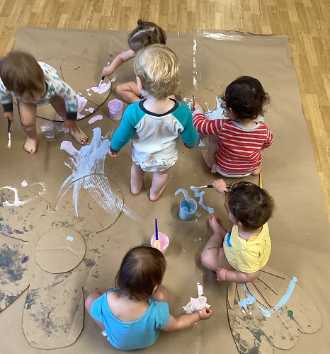 A group of infants painting cardboard flowers on the floor