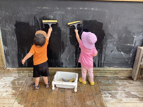 Two children using squeegees on the chalk board outside