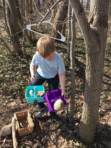 School age child holding 2 baskets attached to a hanger with string attached - the child has 2 roks in one basket and 1 rock in the other looking at the baskets