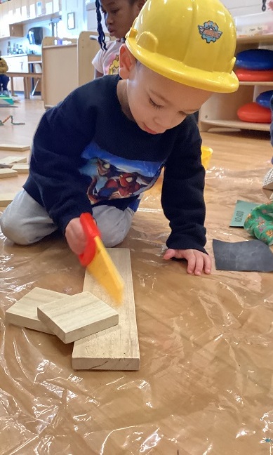 A preschool child using a pretend saw to cut wood