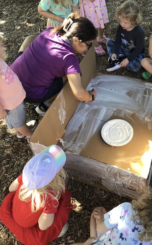6 Preschool children observing an educator painting a big box that will become their Lemonade stand