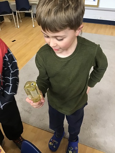 School Age 2 child holding a glass jar filled with water and sparkles and screwed on tightly looking at the piece of foam that says 'yes' floating at the top
