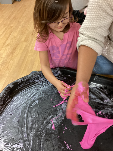 A school aged child and educator exploring sticky pink slime