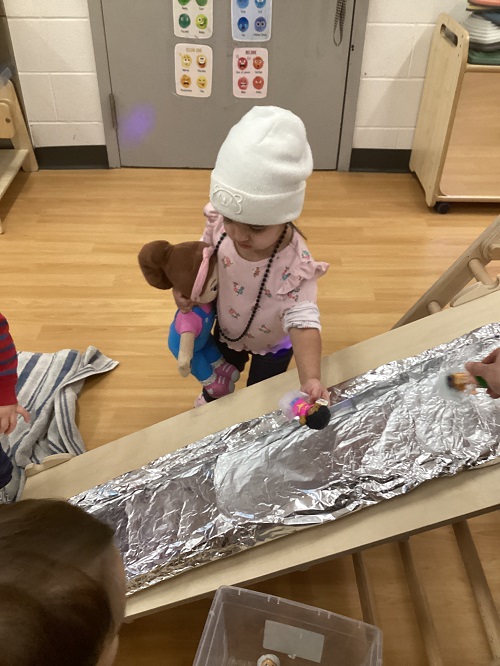 A toddler holding a little people figure overtop of a ramp