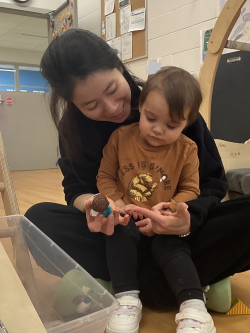 A toddler sitting with an educator looking at little people figures