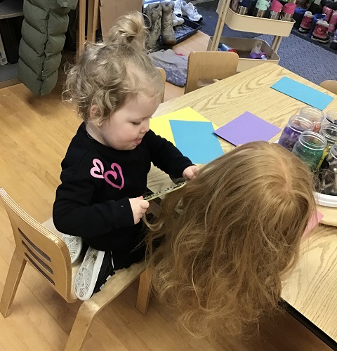 Preschool child sitting at the table combing a mannequin's hair