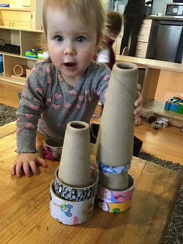 An infant is placing a cone on top of some rings.