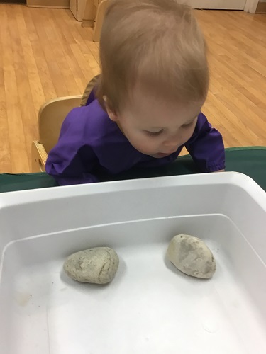 An infant is looking closely at some rocks in a bucket.