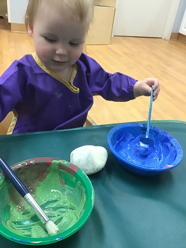 An infant is dipping a sponge in paint.