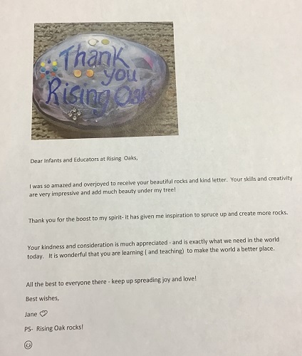 A photo of a rock with, "Thank you RisingOaks," written on it. With a letter thanking the infant room for adding rocks to a neighbours rock garden.