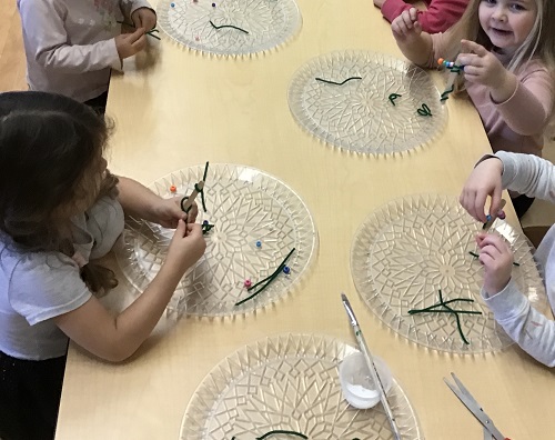 Several preschoolers are adding beads to pipe cleaners to make ornaments. 