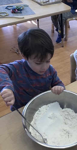 A preschooler is stirring some flour in a bowl.