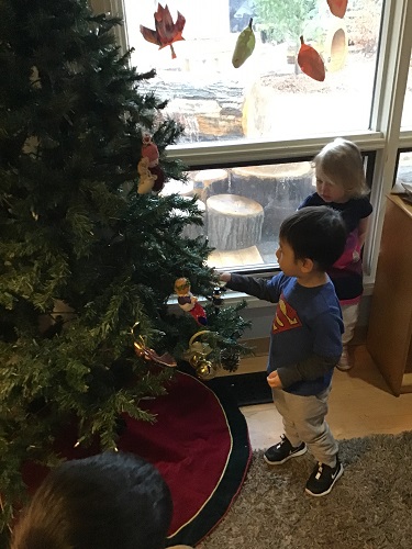 Two preschool children are adding ornaments to their Christmas tree.