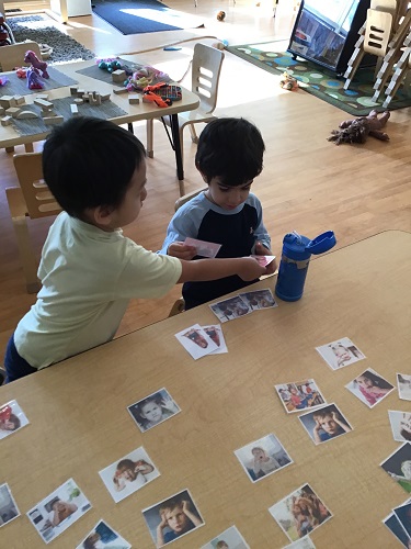 One preschooler is showing another preschooler a picture with a child expressing an emotion.